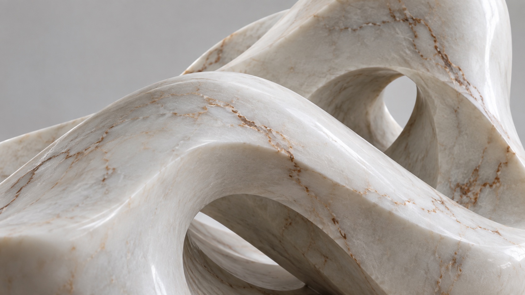 A close view of the smooth curves of a white veined marble sculpture where two folds cross.