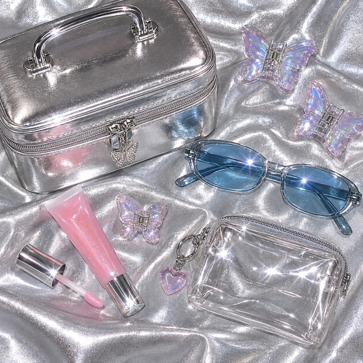 Frosted lip gloss, chrome compacts and translucent cosmetic cases sit in a glossy Y2K vanity arrangement.